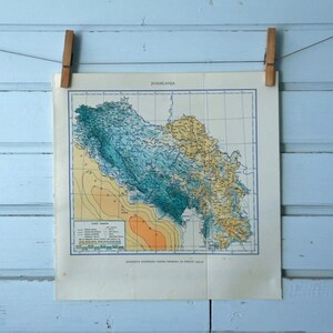 Puede incluir: Impresión de mapa antiguo de una región geográfica, con tonos de azul, verde, amarillo y naranja. El mapa está suspendido por pinzas de madera sobre un fondo de madera azul claro. El título del mapa es visible en la parte superior.