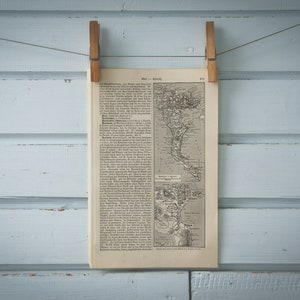 May include: A black and white map of the Americas, printed on a page of a book. The map is hanging on a light blue wall with wooden clothes pegs.