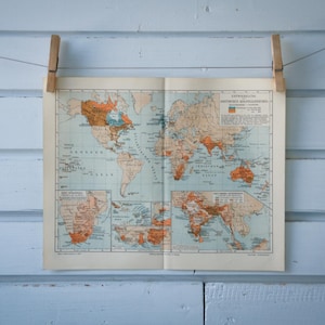 Puede incluir: Un mapa del mundo vintage impreso en papel, colgado en una pared azul claro con dos pinzas de madera.