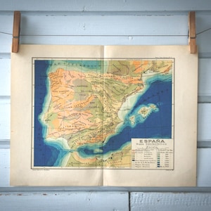 Puede incluir: Mapa antiguo de España, que muestra la Península Ibérica. El mapa, impreso en papel envejecido, utiliza un código de colores para representar el terreno, con el azul indicando el mar. El mapa está sujeto con pinzas de madera.