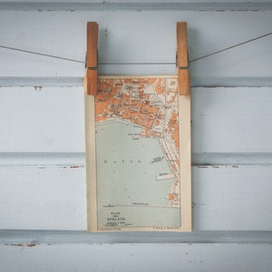May include: A vintage map of the city of Spalato, Croatia, hanging on a white wooden wall with two wooden clothes pegs.