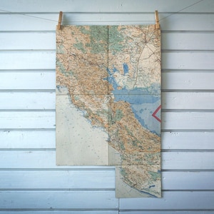 May include: Vintage map of California, displayed on a clothesline with wooden clothespins against a light blue wooden wall. The map features detailed geographical information, including coastlines, rivers, and cities, with a red triangle marking a location.