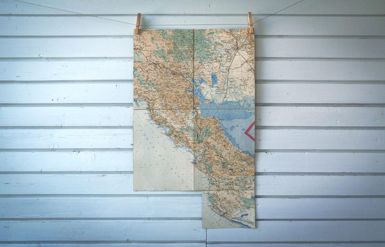 May include: Vintage map of California, displayed on a clothesline with wooden clothespins against a light blue wooden wall. The map features detailed geographical information, including coastlines, rivers, and cities, with a red triangle marking a location.