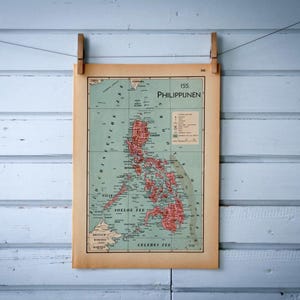 Puede incluir: Mapa antiguo de Filipinas, exhibido en una pared de madera azul claro. El mapa está impreso en papel envejecido y sujeto por dos pinzas de madera. El mapa presenta colores rojo y verde, con el texto "PHILIPPINEN" visible.