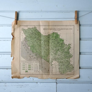 Può includere: Una mappa vintage, stampata su carta invecchiata, è sospesa con mollette di legno contro un muro di legno azzurro. La mappa presenta dettagli geografici verdi e grigi, con del testo visibile.