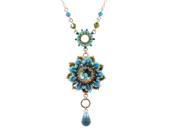 May include: A gold-toned necklace featuring a floral pendant with turquoise and blue beads. The necklace has a delicate chain and a smaller circular pendant above the floral design. A teardrop-shaped bead hangs below the floral pendant.