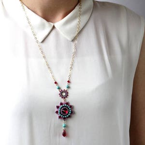 May include: A gold chain necklace with a turquoise and red beaded pendant featuring a flower design.