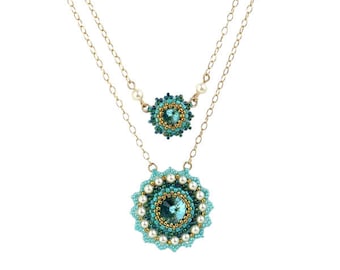 May include: A gold chain necklace with two turquoise and gold beaded pendants. The larger pendant is a round design with a large turquoise crystal in the center. The smaller pendant is a smaller version of the larger pendant.