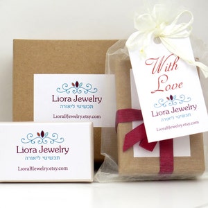 May include: Two brown cardboard boxes with a white label that says "Liora Jewelry" in English and Hebrew. The smaller box is in a clear organza bag with a red ribbon and a white tag that says "With Love" and "Liora Jewelry" in English and Hebrew.