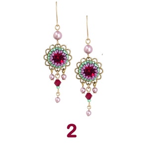 May include: A pair of gold dangle earrings with pink and green beads, a red crystal center, and a pink bead at the top of each earring.
