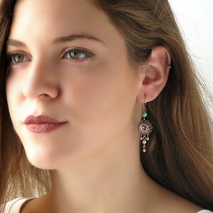 May include: Gold dangle earrings with a pink and turquoise floral design. The earrings feature a round, beaded centerpiece with a pink stone in the center. The earrings are accented with small, pink and turquoise beads.