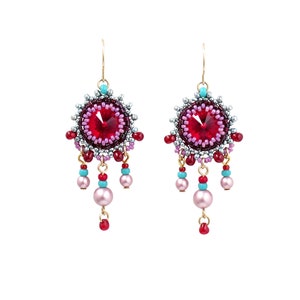 May include: A pair of dangle earrings with a red crystal center surrounded by pink, purple, and silver beads. The earrings have a gold hook and dangle with pink, red, and turquoise beads.
