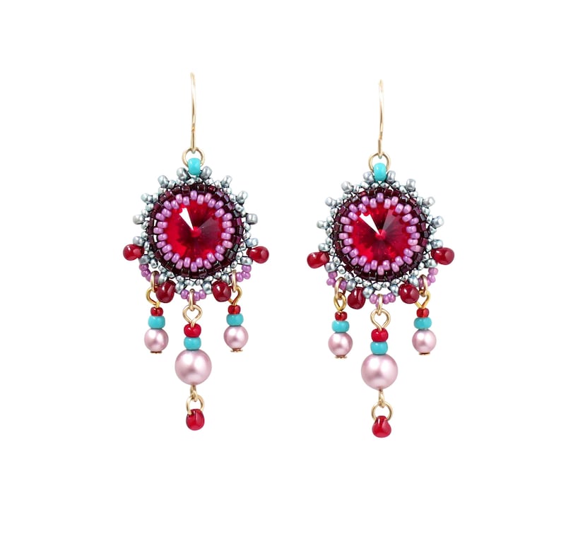 May include: A pair of dangle earrings with a red crystal center surrounded by pink, purple, and silver beads. The earrings have a gold hook and dangle with pink, red, and turquoise beads.
