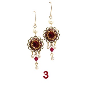 May include: A pair of gold earrings with red and gold beaded flower accents and dangling red and white beads.