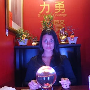 Amanda looking at the camera with a welcoming smile, holding up a selection of tarot cards against a cozy backdrop of glowing candles and crystals.