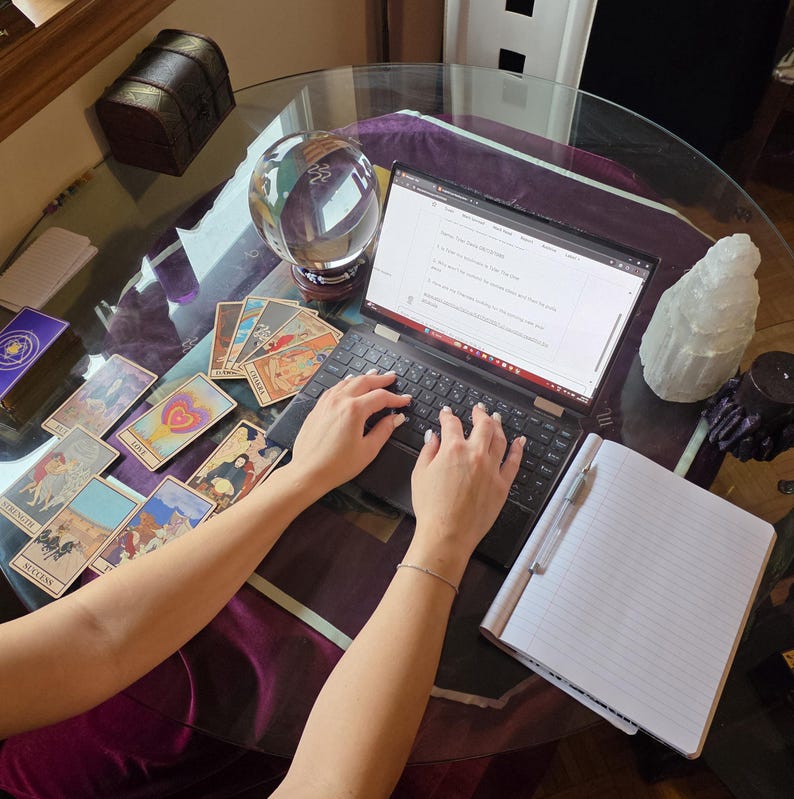 High-angle photo of Amanda analyzing a complex tarot card spread on a table decorated with raw amethyst crystals and a burning stick of incense.