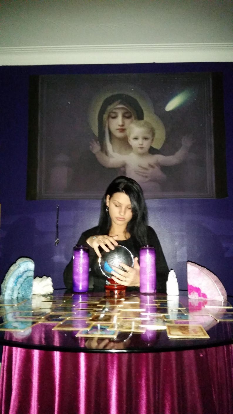 Portrait of Amanda sitting at her reading table with her hands gently resting near a glass crystal ball, ready to connect with intuitive energy.