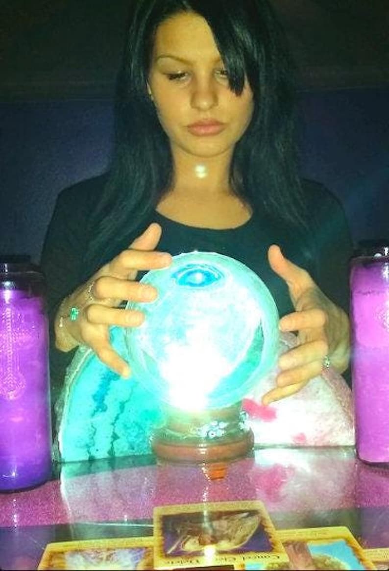 Candid photo of Psychic Amanda smiling warmly in her cozy reading room, with gentle trails of incense smoke drifting peacefully in the background.