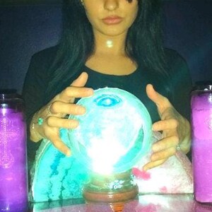 Candid photo of Psychic Amanda smiling warmly in her cozy reading room, with gentle trails of incense smoke drifting peacefully in the background.