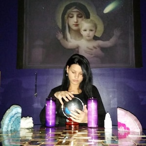 Portrait of Amanda sitting at her reading table with her hands gently resting near a glass crystal ball, ready to connect with intuitive energy.