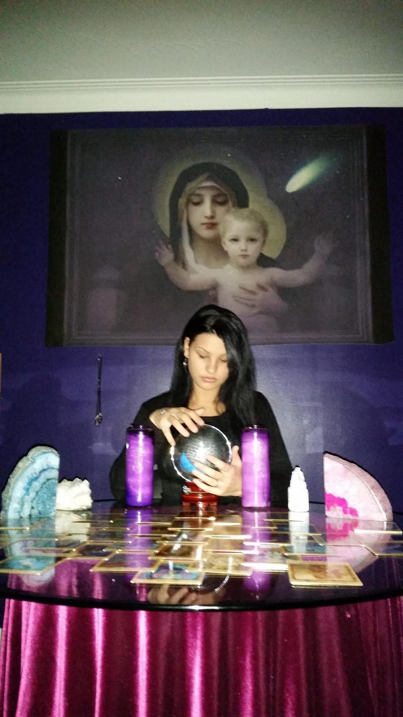Portrait of Amanda sitting at her reading table with her hands gently resting near a glass crystal ball, ready to connect with intuitive energy.