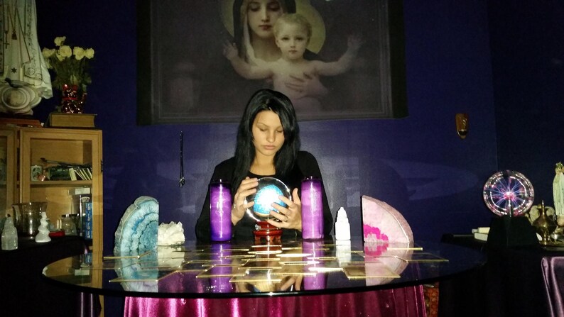 Warm portrait of Psychic Amanda holding a large, polished crystal while smiling at the camera in a soft-lit, peaceful spiritual space.