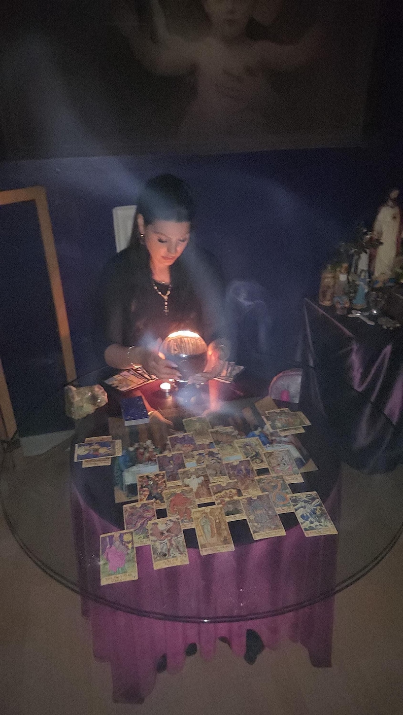 High-angle photo of Amanda analyzing a complex tarot card spread on a table decorated with raw amethyst crystals and a burning stick of incense.