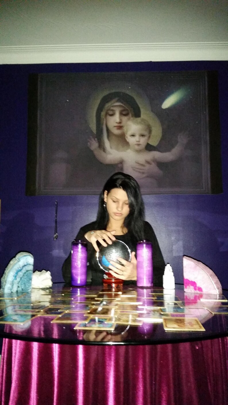 Portrait of Amanda sitting at her reading table with her hands gently resting near a glass crystal ball, ready to connect with intuitive energy.
