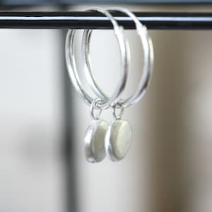May include: A pair of silver hoop earrings with a hammered texture. Each hoop has a small, round, silver charm attached.
