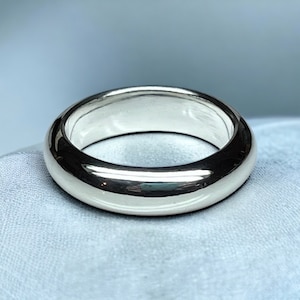 May include: A smooth, silver-toned wedding band with a rounded profile.