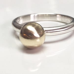 K&ouml;nnte beinhalten: Ein Silberring mit einer goldenen Kugel oben drauf.