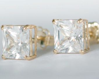 May include: A pair of gold earrings with square-shaped clear cubic zirconia stones.