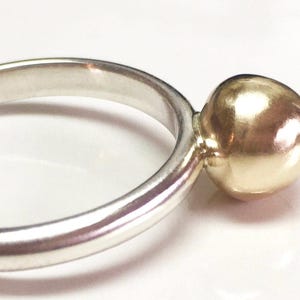 K&ouml;nnte beinhalten: Ein silberner Ring mit einer goldenen Kugel am Ende.