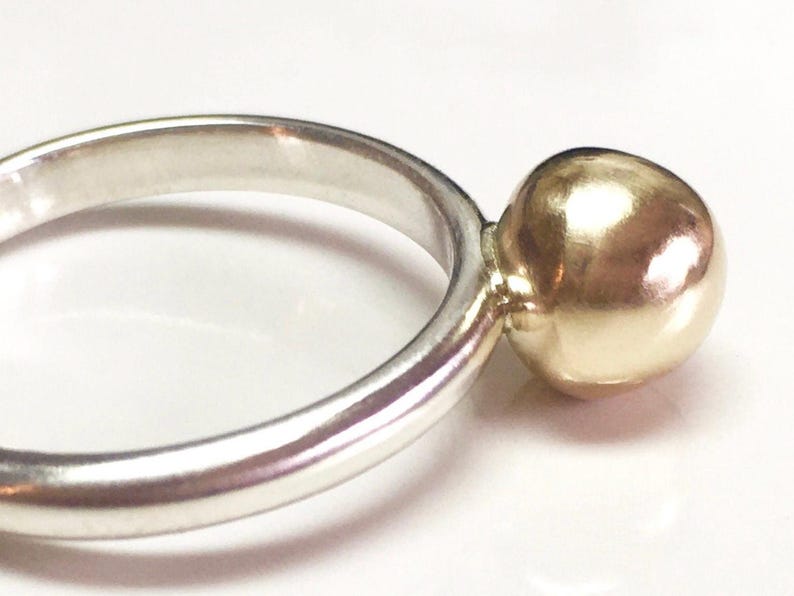 K&ouml;nnte beinhalten: Ein silberner Ring mit einer goldenen Kugel am Ende.