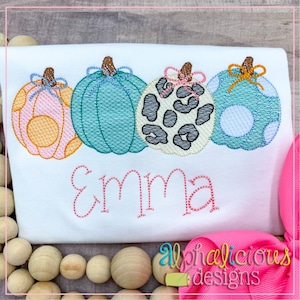 May include: Embroidered design of four pumpkins with bows and the name "Emma" in pink thread on a white t-shirt.