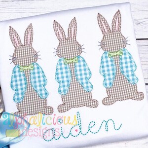 May include: Three brown and white checkered bunnies with blue and white checkered jackets and green bow ties. The bunnies are standing in a row. The text "aphalicious designs" and "auden" is stitched below the bunnies.