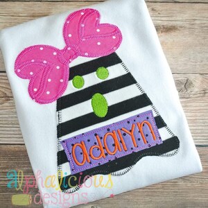 May include: A black and white striped ghost with a pink polka dot bow and green eyes. The ghost has a purple and black polka dot name tag with the name "adaiyn" embroidered in orange.