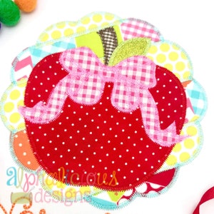 May include: A red apple with white polka dots and a pink gingham bow. The apple is surrounded by a colorful patchwork of fabric with a scalloped edge.