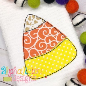 May include: A felt applique of a candy corn with a white, orange, and yellow design. The candy corn is outlined in black thread.