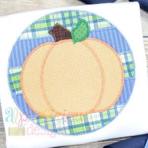 May include: A round applique featuring a pumpkin with a green stem and leaves. The pumpkin is surrounded by a blue and green plaid fabric.