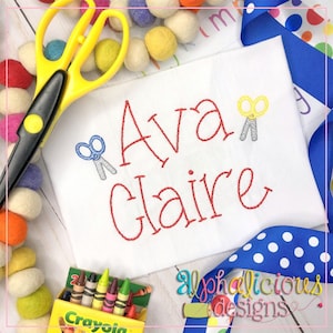 May include: White fabric with the names "Ava" and "Claire" embroidered in red thread. Small embroidered scissors in blue and yellow accent the names. A box of crayons and a pair of yellow scissors are also visible.