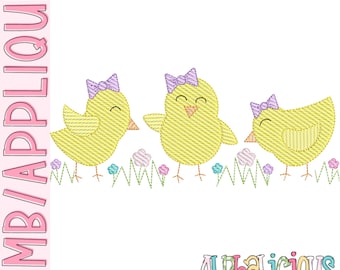 May include: Three yellow chicks with purple bows stand in a row on a green grass background with pink flowers. The chicks are embroidered with a textured pattern. The text "Alphalicious Designs" is at the bottom of the image.