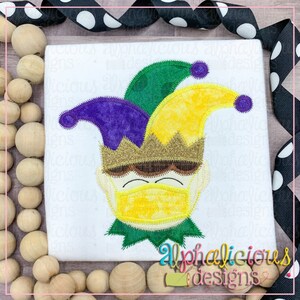 May include: A colorful felt applique of a jester wearing a yellow, green, and purple hat with a gold crown and a yellow face mask. The jester has brown eyes and a brown mouth.