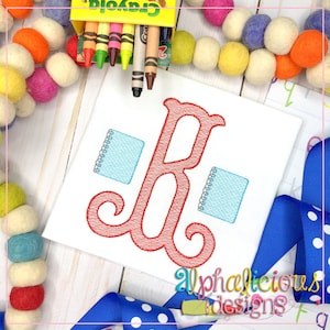 Puede incluir: Tela cuadrada blanca con una letra "B" roja bordada y dos cuadernos azul claro. Una caja de crayones Crayola está en la parte superior. El texto "Alphalicious Designs" está en la parte inferior.