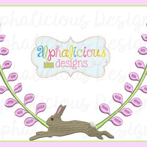 Peut inclure: Broderie représentant un lapin brun sautant à travers une couronne de fleurs roses. Le motif comprend le texte "alphaelicious designs".