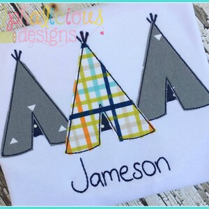 Könnte beinhalten: Ein weißes T-Shirt mit drei gestickten Tipis in verschiedenen Mustern. Die Tipis sind grau, kariert und grau. Der Name "Jameson" ist unter den Tipis gestickt.