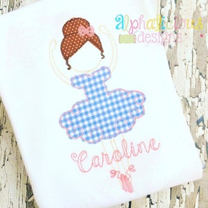 May include: Embroidered design of a ballerina with brown hair, a blue and white gingham dress, and pink shoes. The name "Caroline" is embroidered below the ballerina.