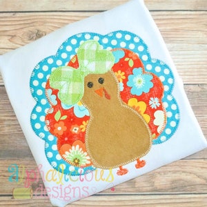May include: A brown felt turkey with a green and white plaid bow on its head. The turkey is surrounded by a blue and white polka dot fabric with a floral pattern.