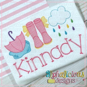 May include: Embroidered design featuring pink rain boots with yellow bows, a pink umbrella, and a cloud with colorful raindrops. The name "Kinnady" is embroidered in pink. The design is on a white background with the text "Alphalicious designs".