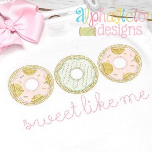 May include: Three embroidered donuts in pink, green, and white with gold accents. The donuts are arranged in a row with the text "sweet like me" stitched in pink below them.